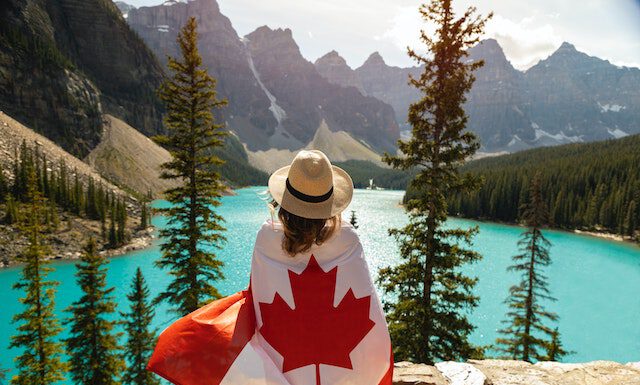 Czy warto lecieć do Kanady? Z czego słynie Kanada? Kobieta z flagą Kanady nad brzegiem jeziora