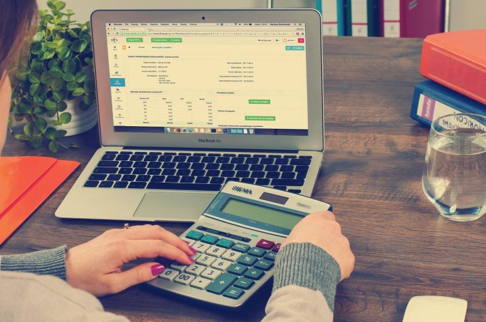 Kobieta oblicza wydatki na kalkulatorze przy laptopie z arkuszem finansowym